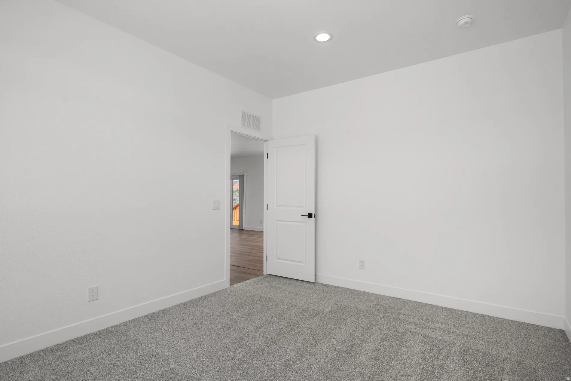 Carpeted room with white walls, recessed ceiling lighting, and a white door with black hardware