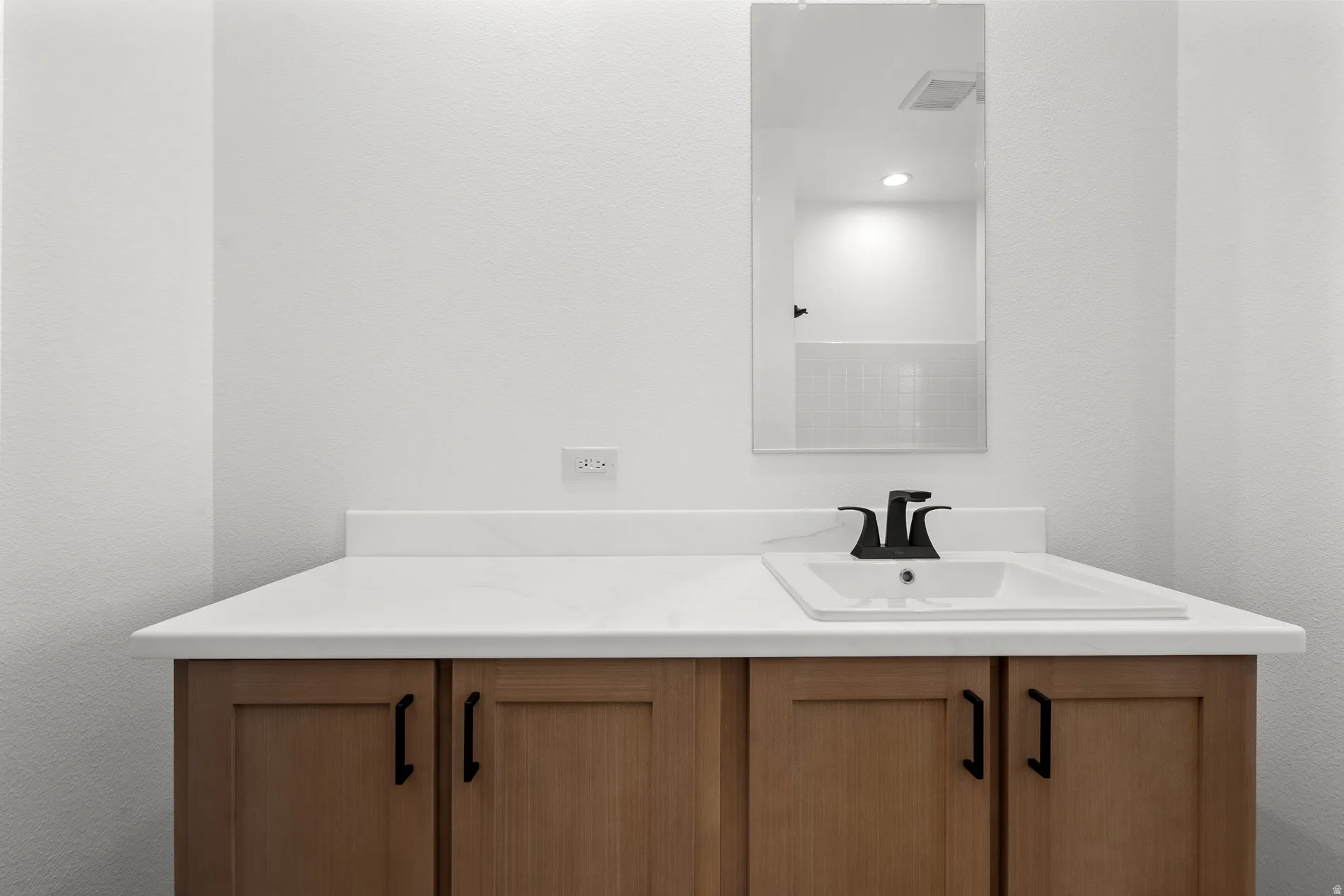 Vanity featuring light wood-finish cabinetry with black hardware, a white countertop, an integrated sink, and a matte black faucet