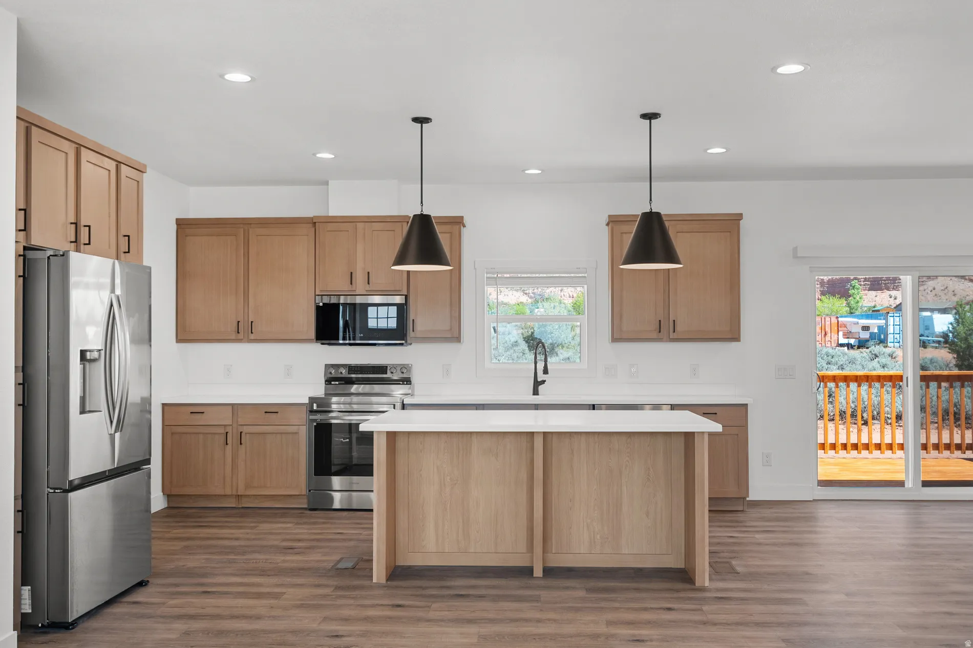 Open-concept kitchen featuring wood-finish cabinetry, stainless steel appliances, and an island with a white countertop