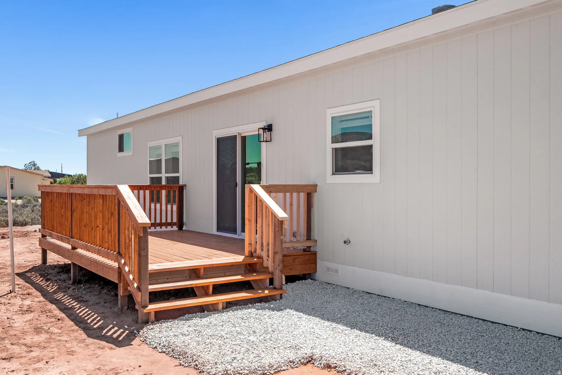 Newly constructed exterior featuring a wooden deck with steps, a sliding glass door, and two windows