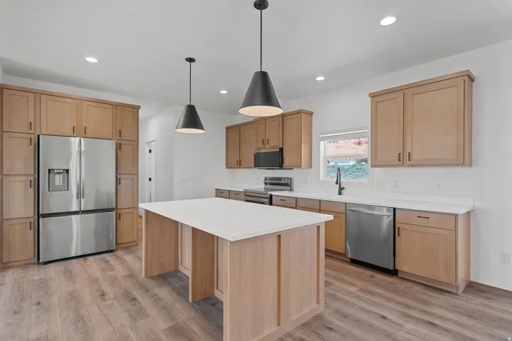 Modern kitchen featuring an expansive center island with a light-toned countertop, wood-finish flooring, recessed lighting, and stylish pendant fixtures