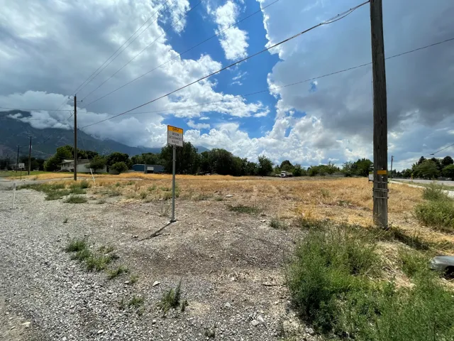Expansive undeveloped land parcel featuring a mountain backdrop and a gravel roadside