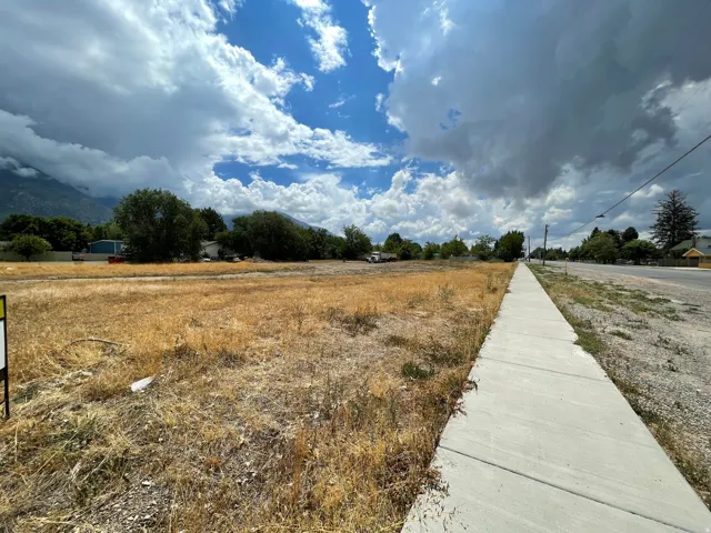 Expansive undeveloped land parcel featuring a paved sidewalk and direct street frontage