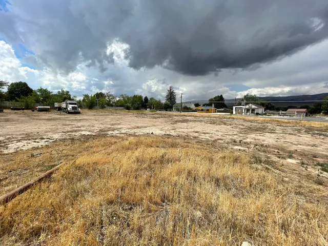 Expansive land parcel featuring a raw earth and dry grass surface, bordered by mature trees and a distant mountainous backdrop