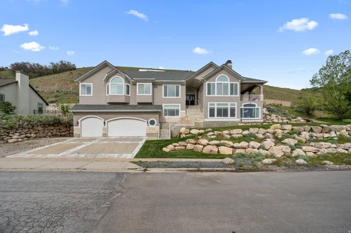Stucco exterior residence featuring an attached four-car garage, multiple bay windows, and a covered upper-level balcony