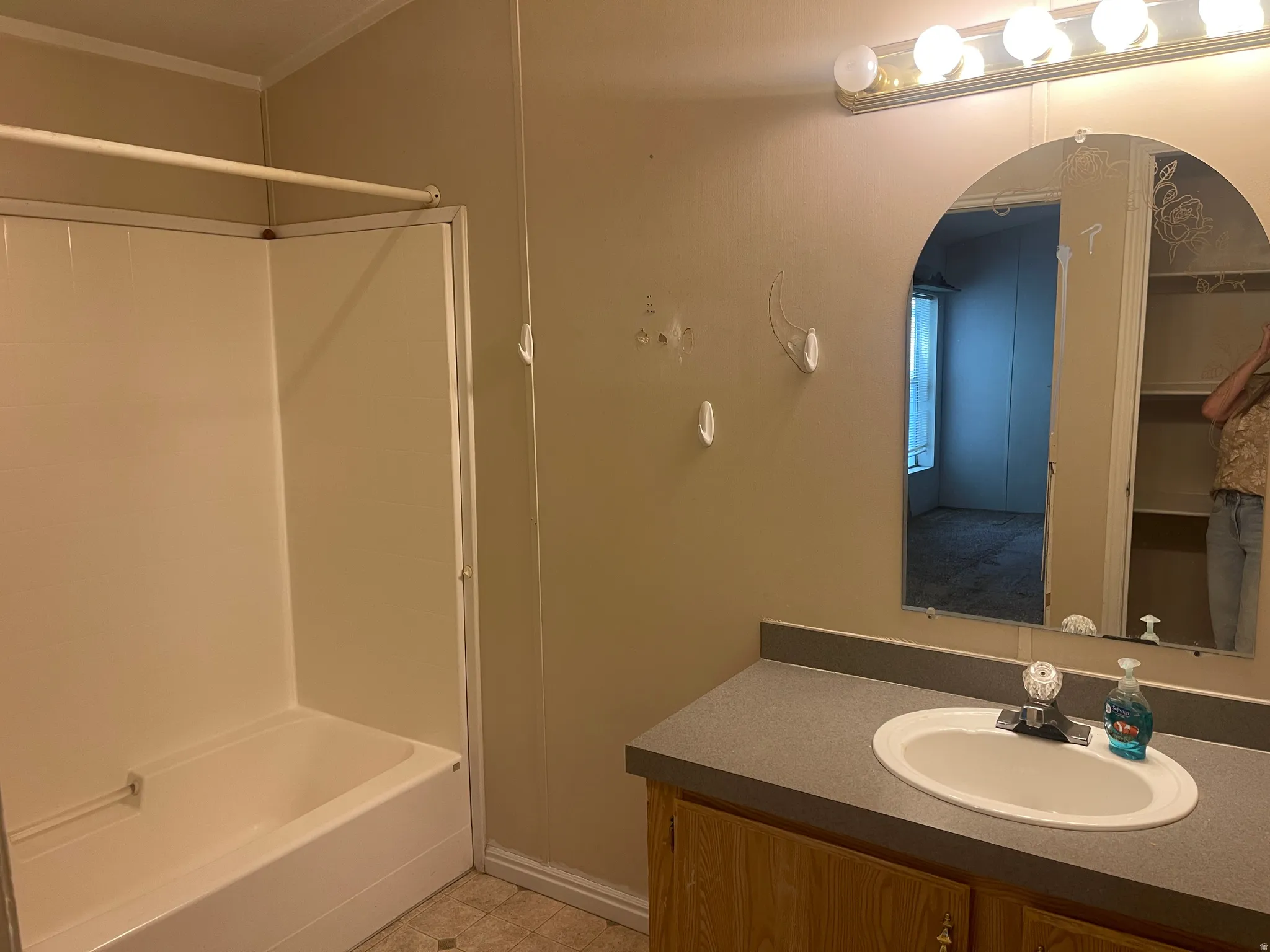 Primary Bathroom featuring a white bathtub and shower surround, a wood-finish vanity with a gray countertop, and an arched mirror with decorative etching