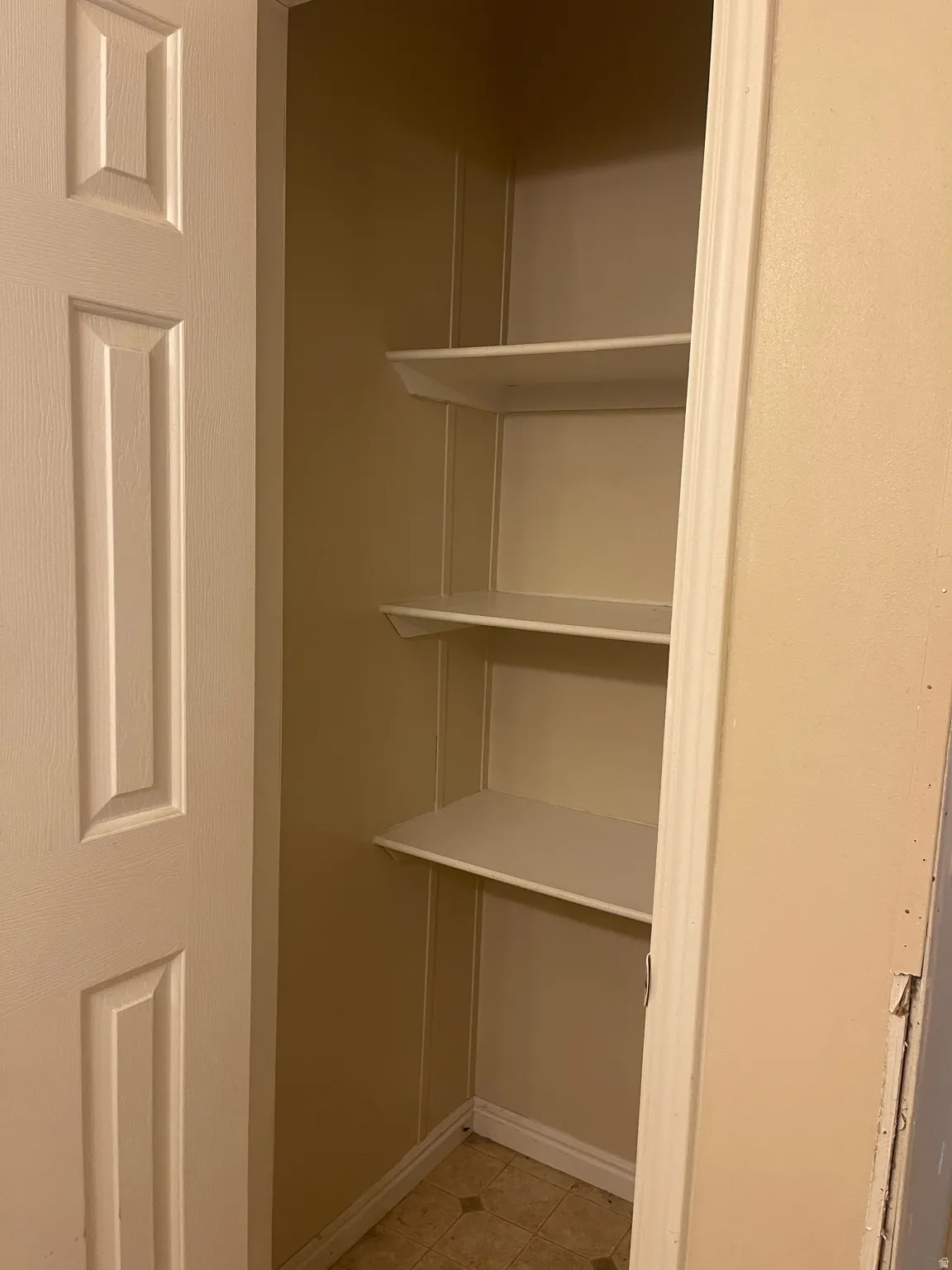 Linen closet primary bedroom featuring three white shelves, a neutral wall color, and patterned floor tile
