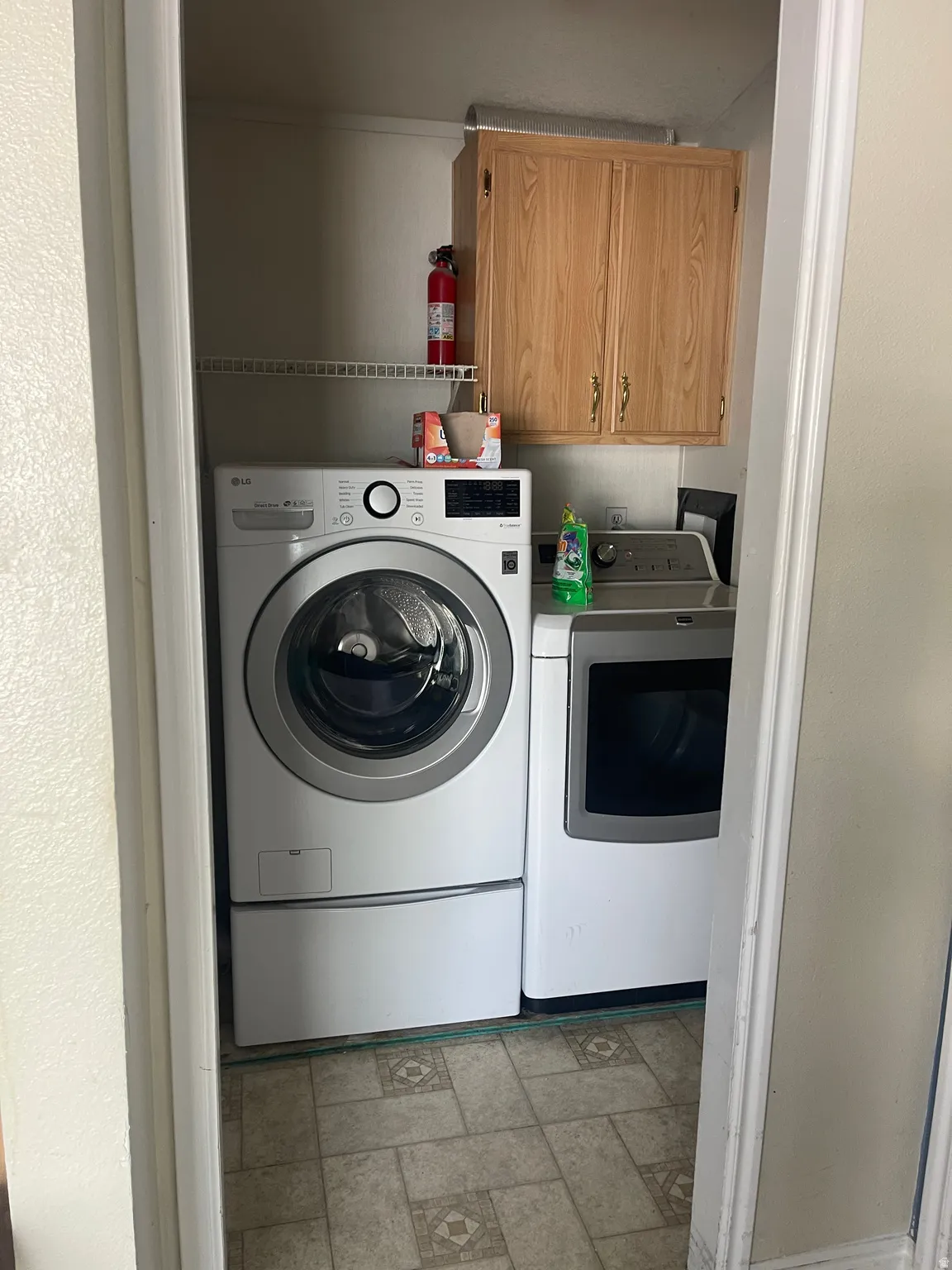 Dedicated laundry area featuring patterned vinyl flooring, overhead wood cabinetry, and a wire shelving unit