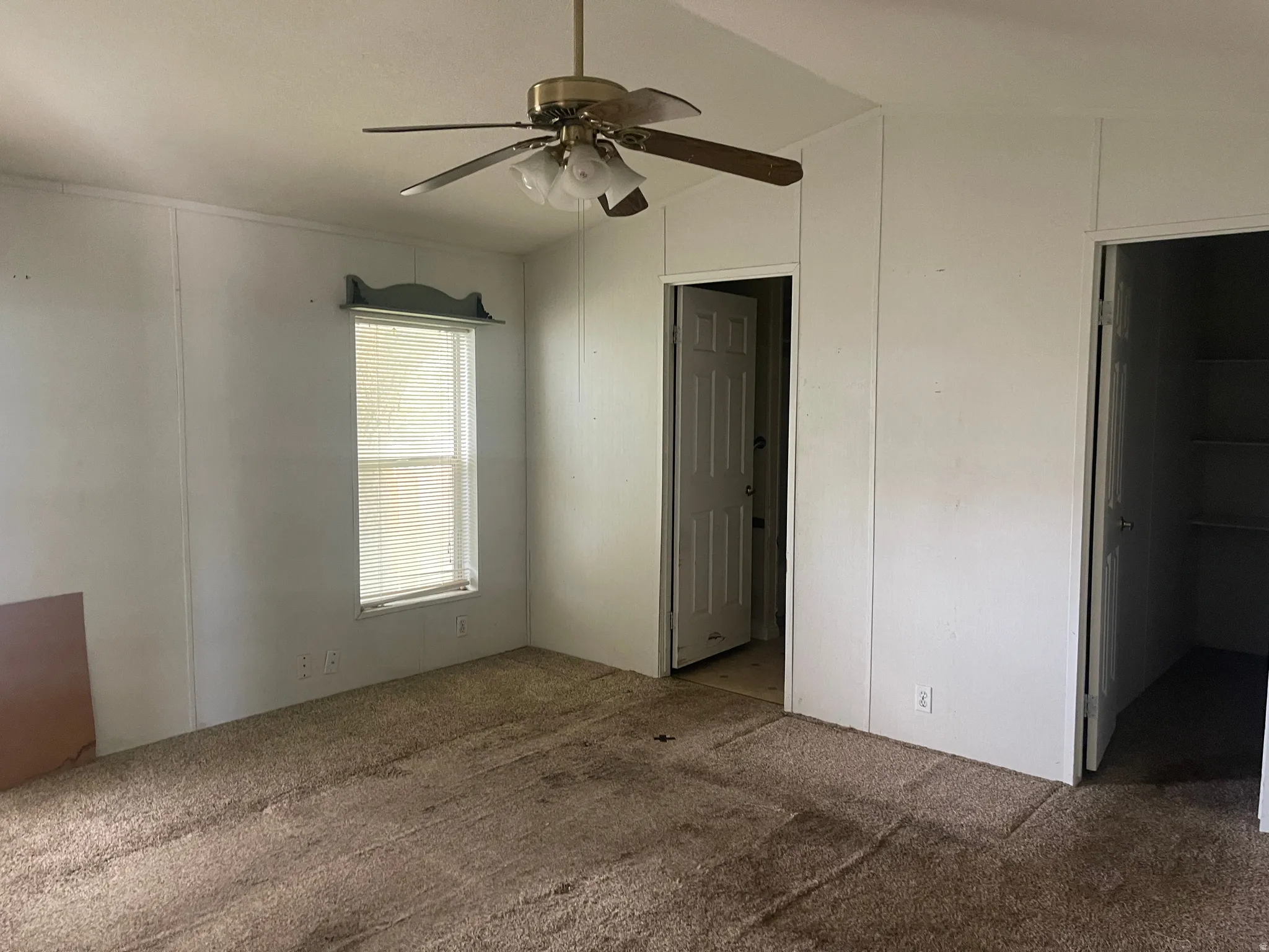 Carpeted primary bedroom with a ceiling fan light fixture, a single window with blinds, and white paneling on the walls