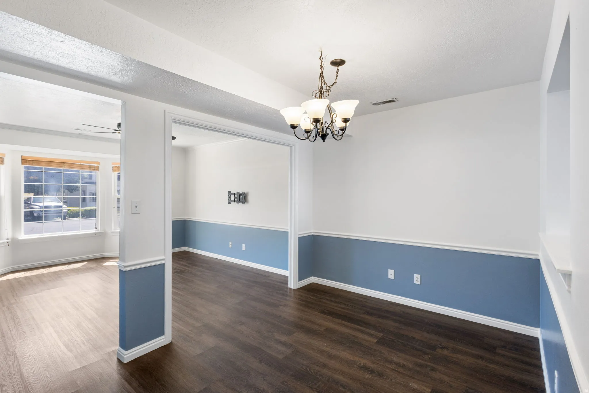 Dining area featuring a bronze chandelier, two-tone wall paint with chair rail molding, and dark wood-finish flooring