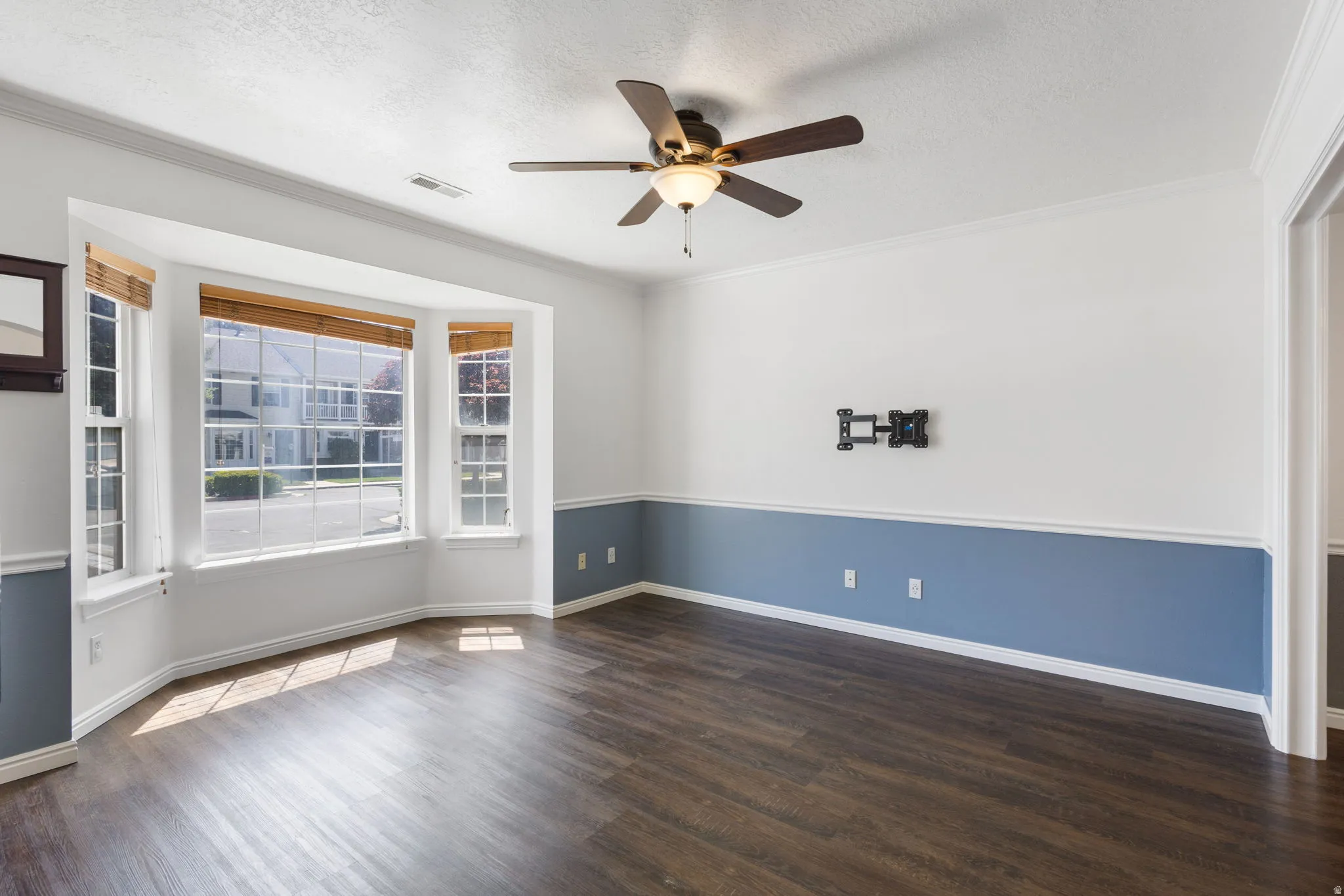 Bay window with multiple panes, wood-finish flooring, two-tone wall treatment with chair rail, ceiling fan with integrated lighting, and crown molding