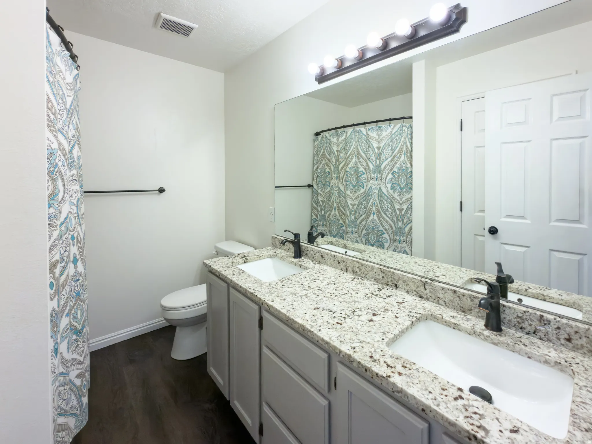 Bathroom featuring a dual vanity with granite-finish countertops, undermount sinks, and matte black fixtures