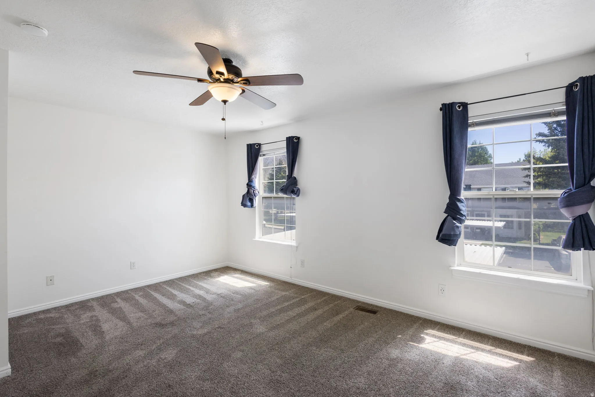 Spacious room featuring neutral carpet flooring, white walls, and a ceiling fan with integrated lighting