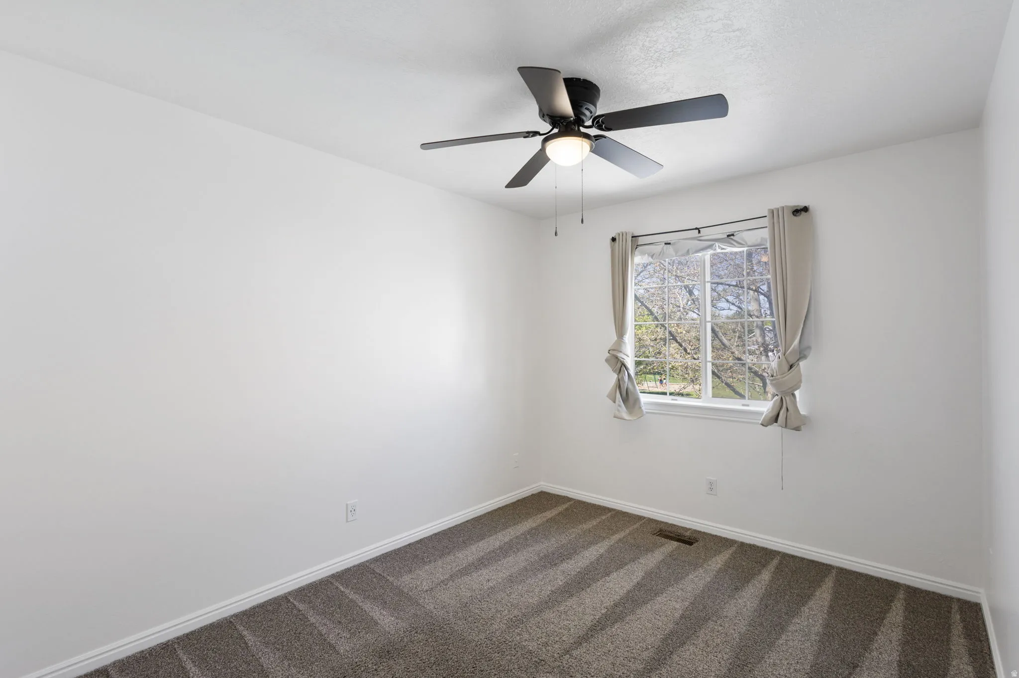 Interior room featuring a ceiling fan with integrated lighting, a window with natural light, and patterned carpeting