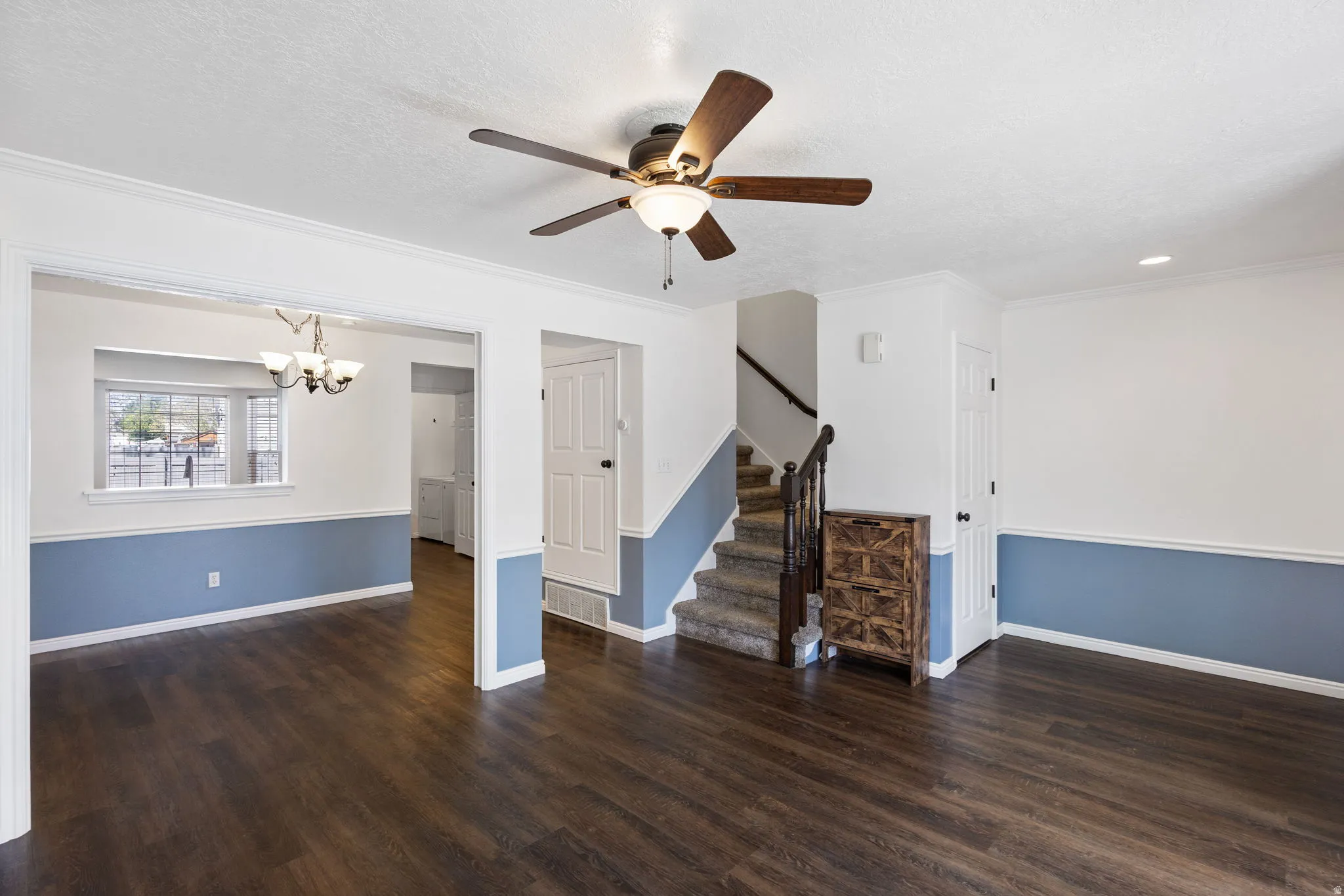 Spacious room featuring wood-finish flooring, a ceiling fan with integrated lighting, and a staircase with dark wood railings