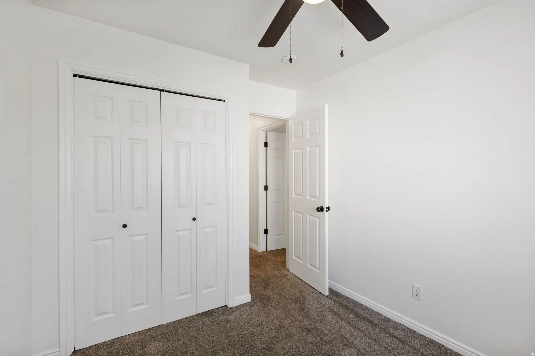 Neutral painted walls featuring a bi-fold closet, dark carpet flooring, and a ceiling fan with light fixture