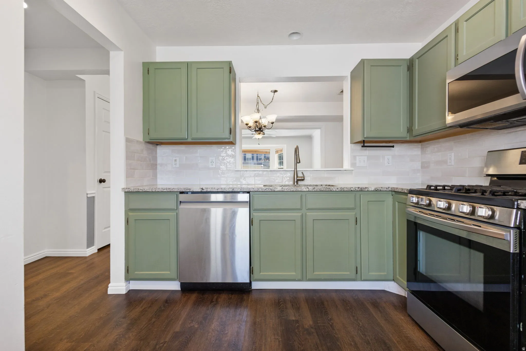 Kitchen featuring sage green cabinetry, stainless steel appliances, a tile backsplash, light-toned countertops, and wood-finish flooring