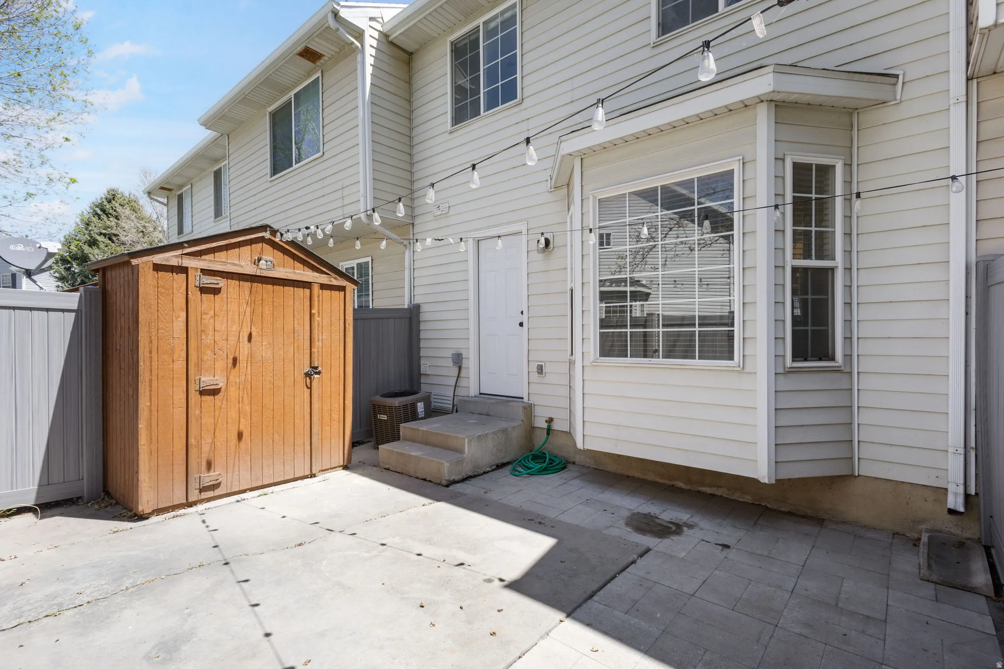 Concrete patio featuring a wood-panel storage shed and bay window