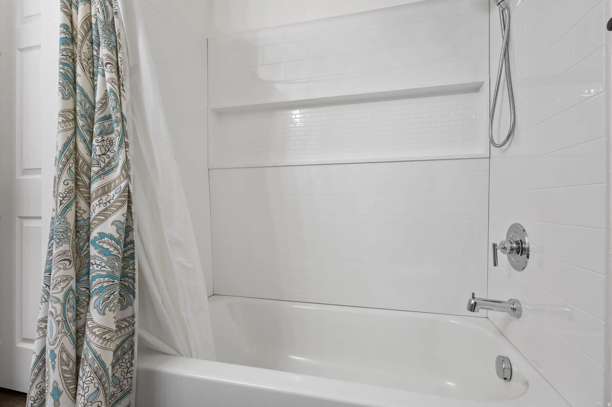 Bathtub with chrome fixtures and white subway tile surround, featuring an integrated shower niche
