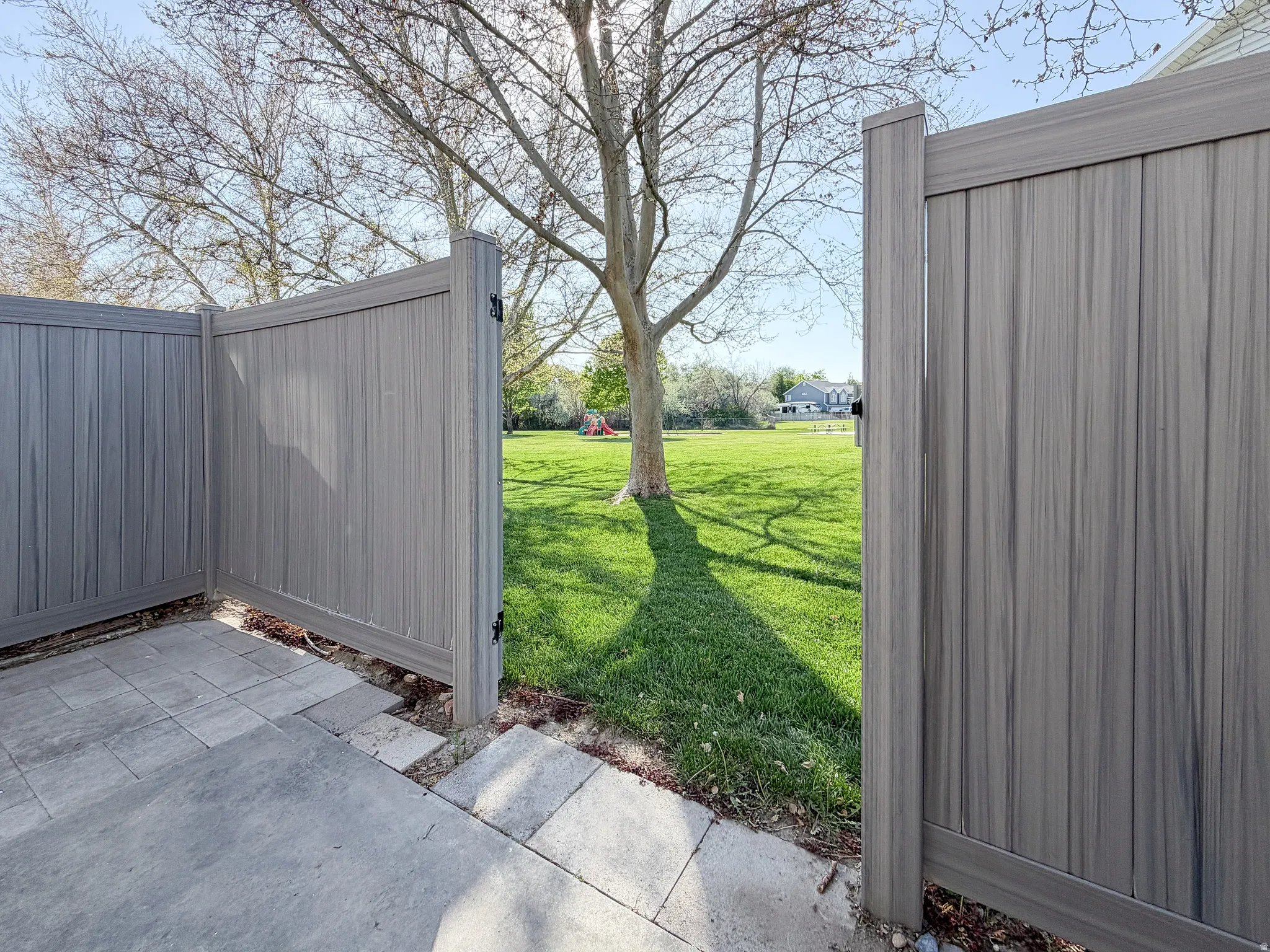 Paved patio area with a privacy fence opening to a manicured lawn and mature trees