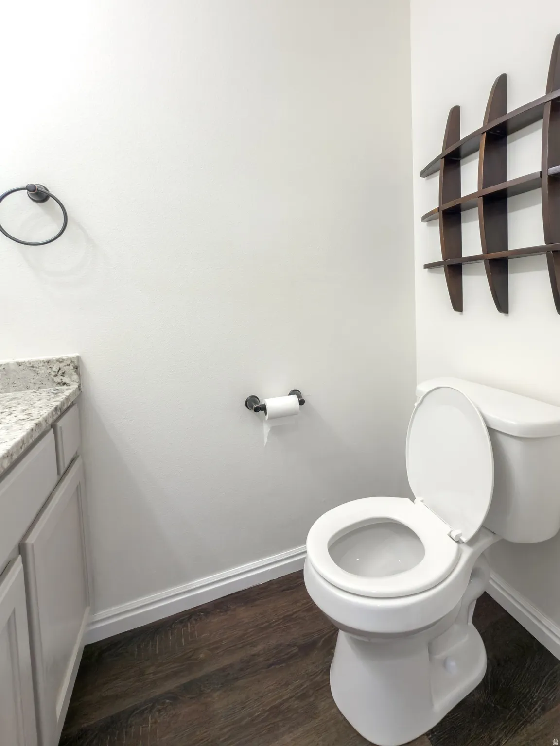 Powder room featuring wood-finish flooring, white baseboards, a white toilet, and a white vanity with a granite-look countertop