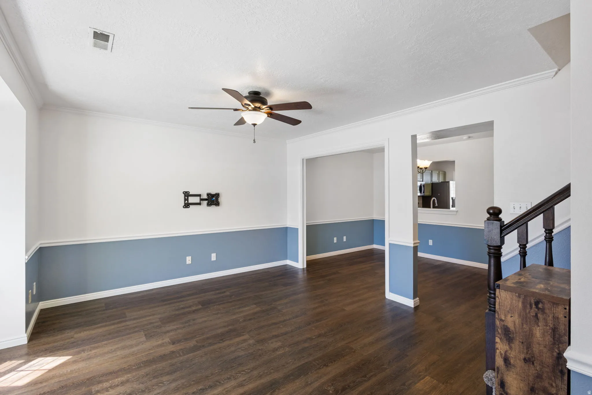 Open concept living area with wood-finish flooring, two-tone wall treatment, and white crown molding