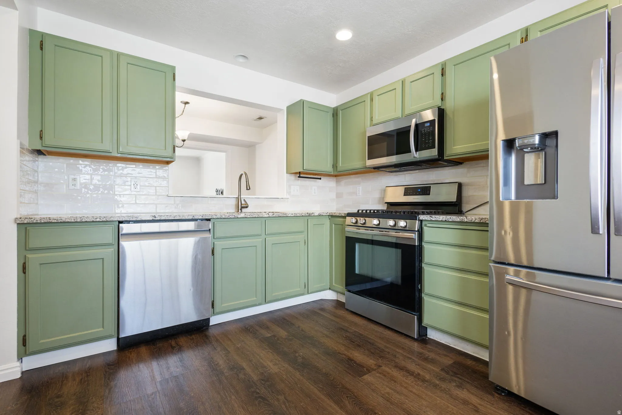 Kitchen featuring sage green cabinetry, stainless steel appliances, speckled countertops, and a white subway tile backsplash