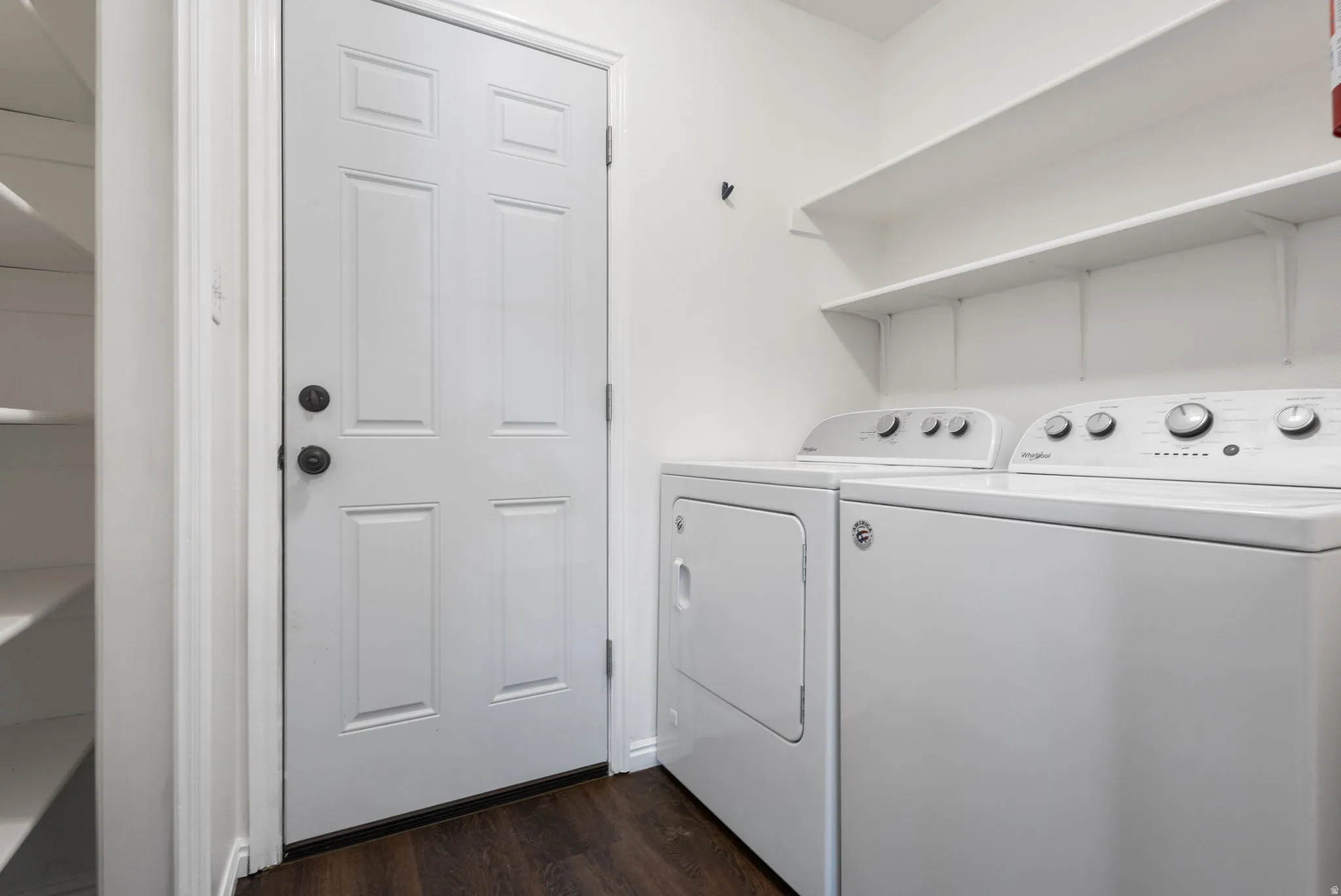 Laundry area with dark wood-finish flooring, white walls, and a white paneled door with black hardware