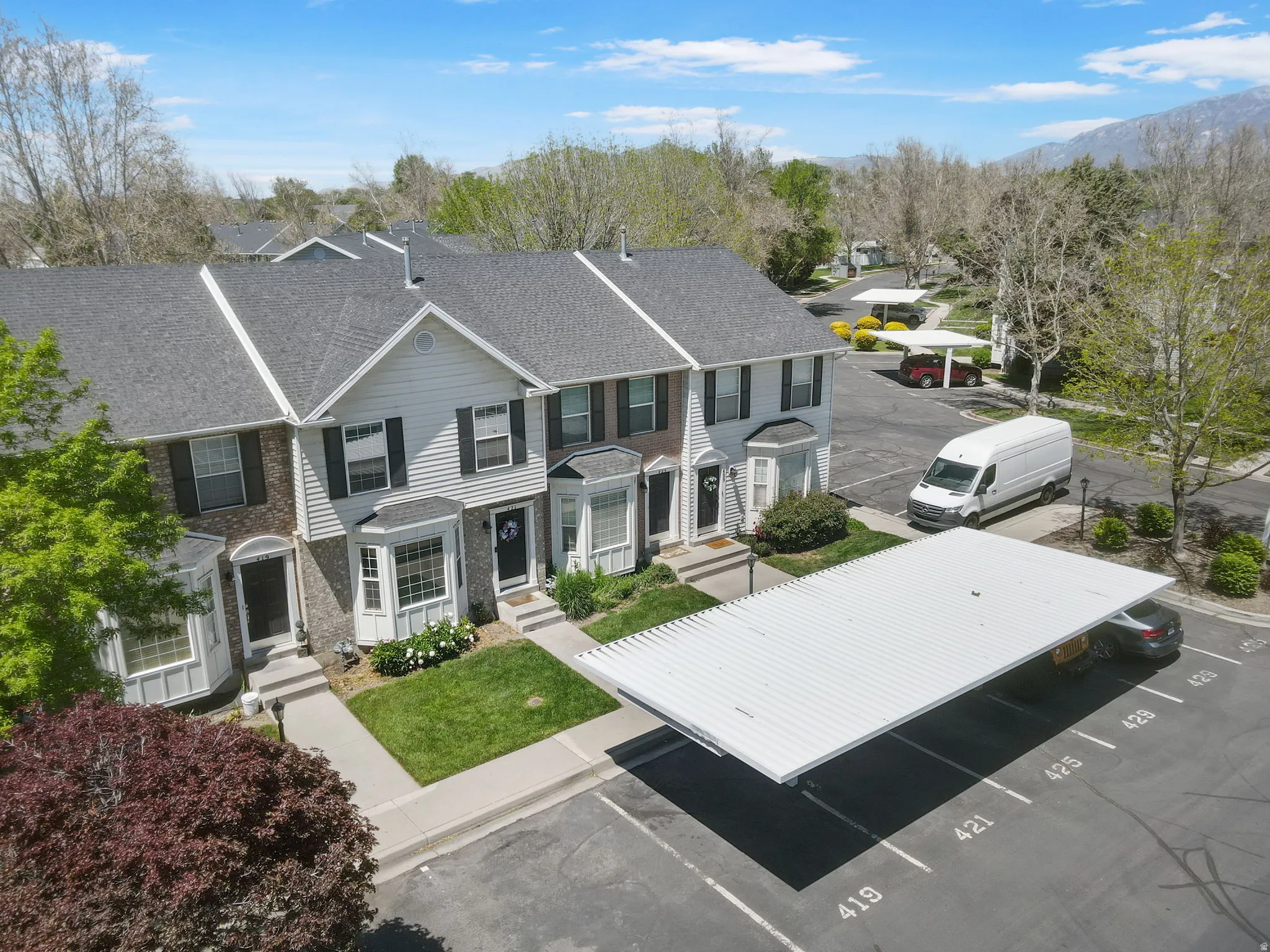 Townhome exterior featuring gray siding, bay windows, dark shutters, and a gray shingle roof