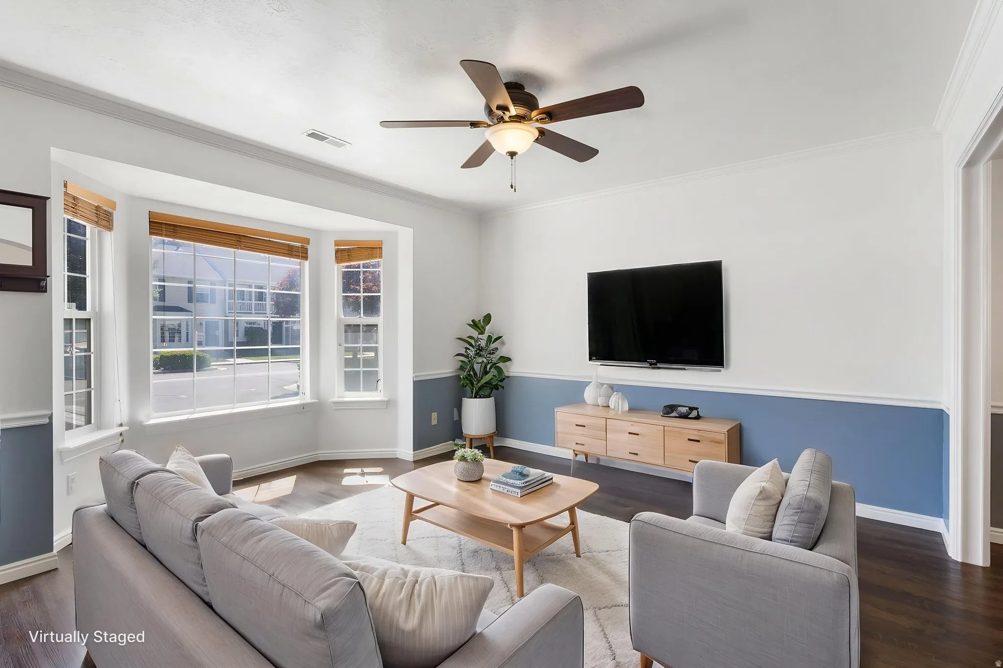 Living area (Virtually staged) featuring a bay window with natural light, wood-finish flooring, a ceiling fan with integrated lighting, and a chair rail molding