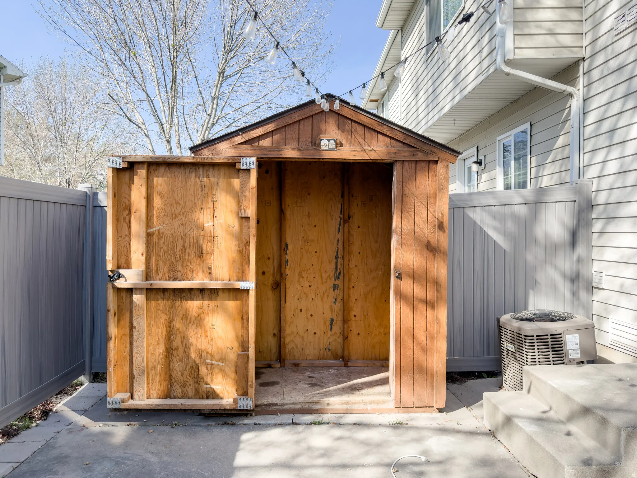 Wood-paneled storage shed with a peaked roof, set on a concrete pad