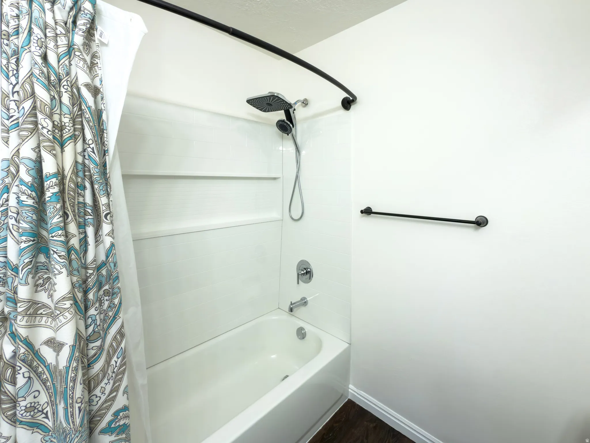 White tub and shower combination with a curved black shower rod, a multi-function showerhead, and integrated shelving