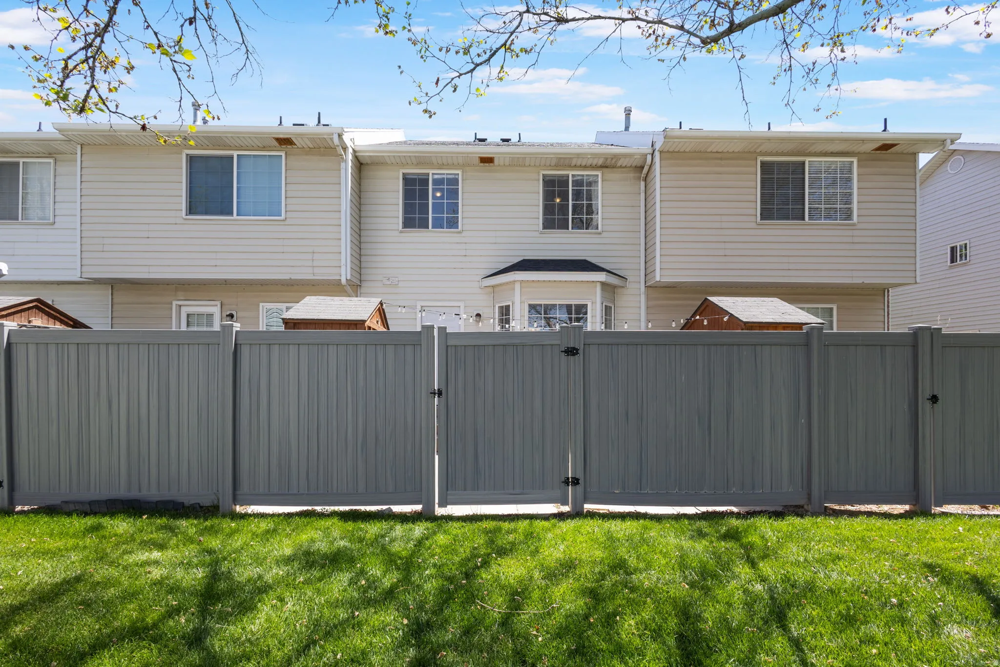 Expansive rear yard featuring a manicured lawn, a full-height privacy fence with gate, and two storage sheds