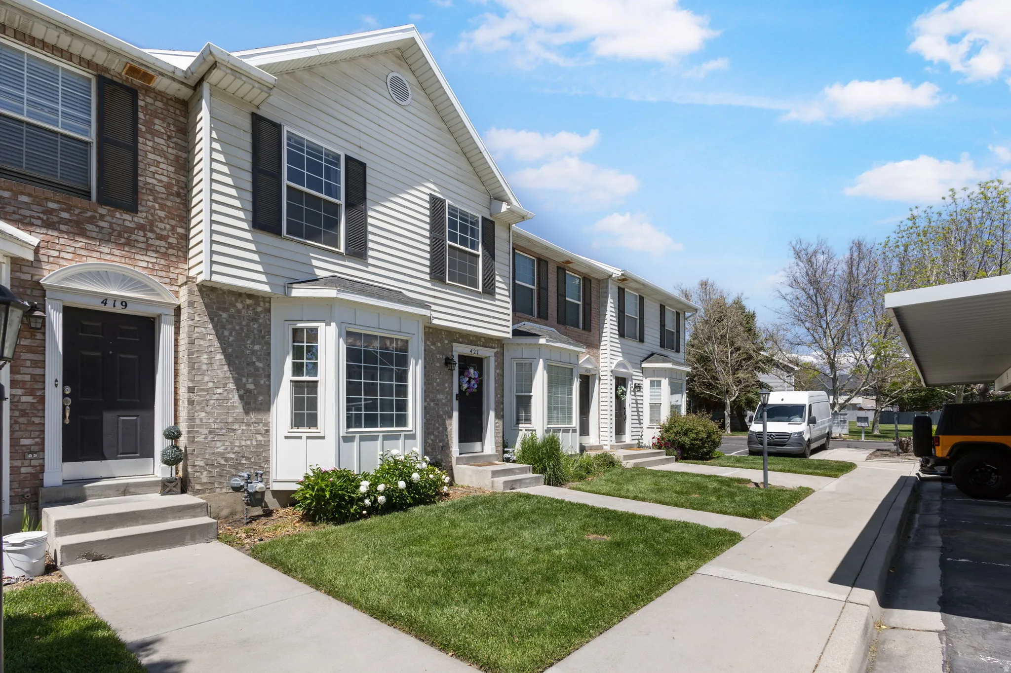 Townhome exterior featuring brick and siding accents, black window shutters, a concrete walkway, and a manicured lawn