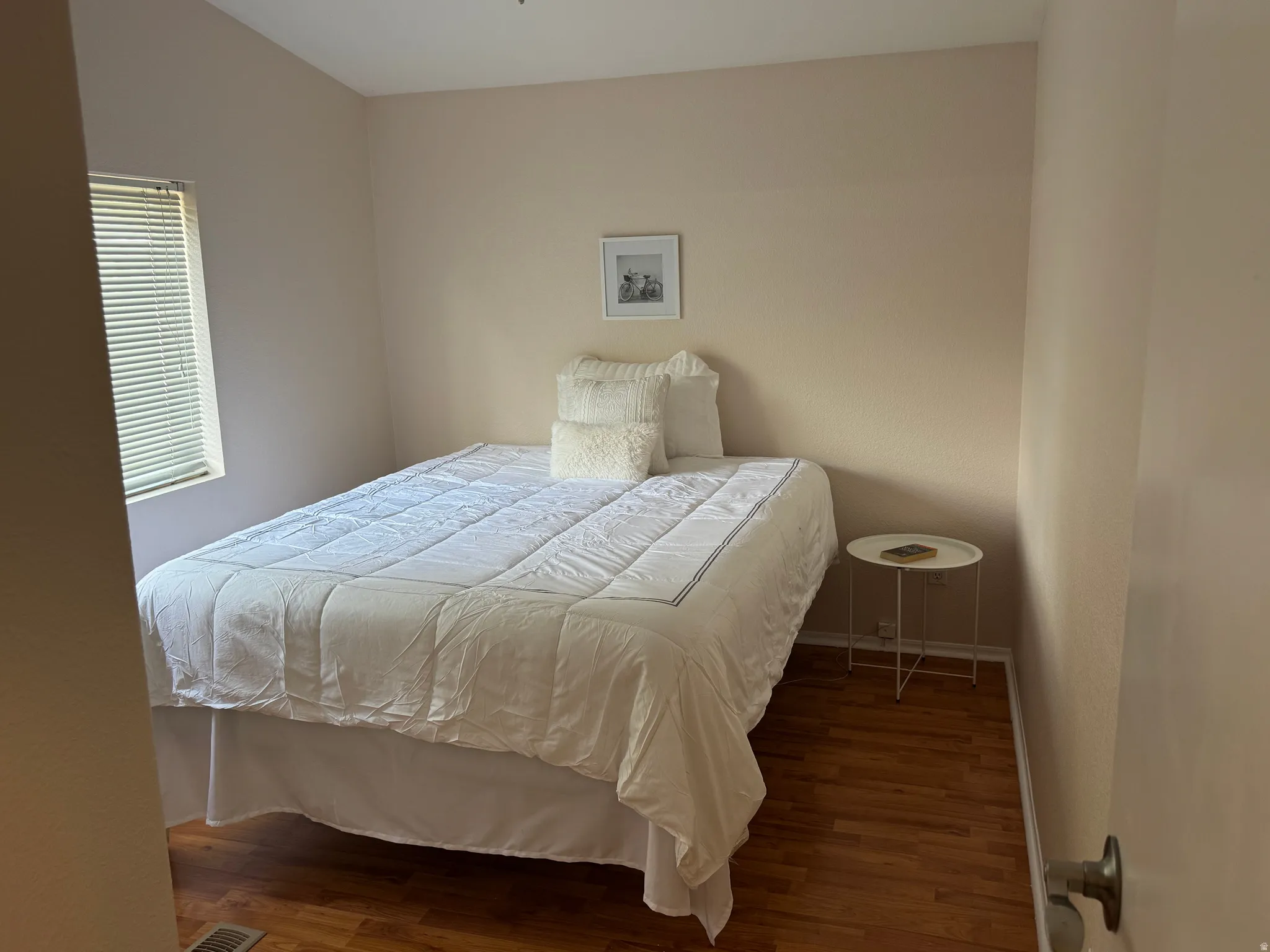 Bedroom featuring neutral wall tones, wood-finish flooring, a window with horizontal blinds, and a ceiling-mounted light fixture