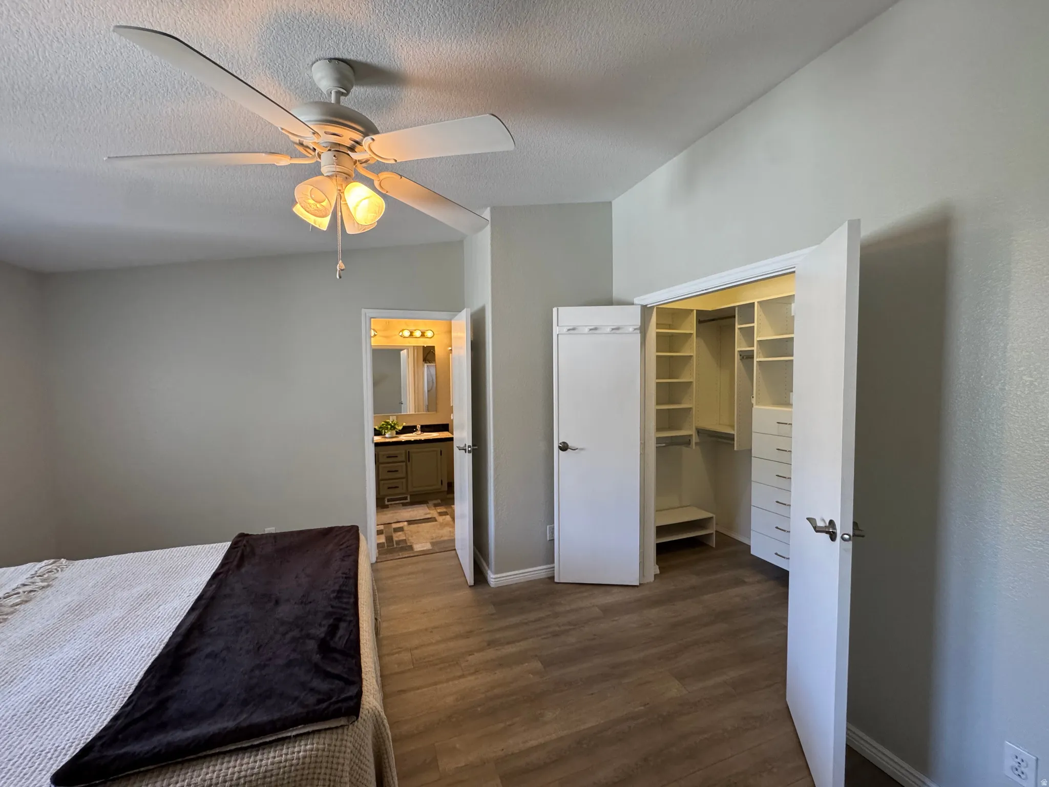 Bedroom featuring wood-finish flooring, a ceiling fan with integrated lighting, and a custom closet system with shelving and drawers