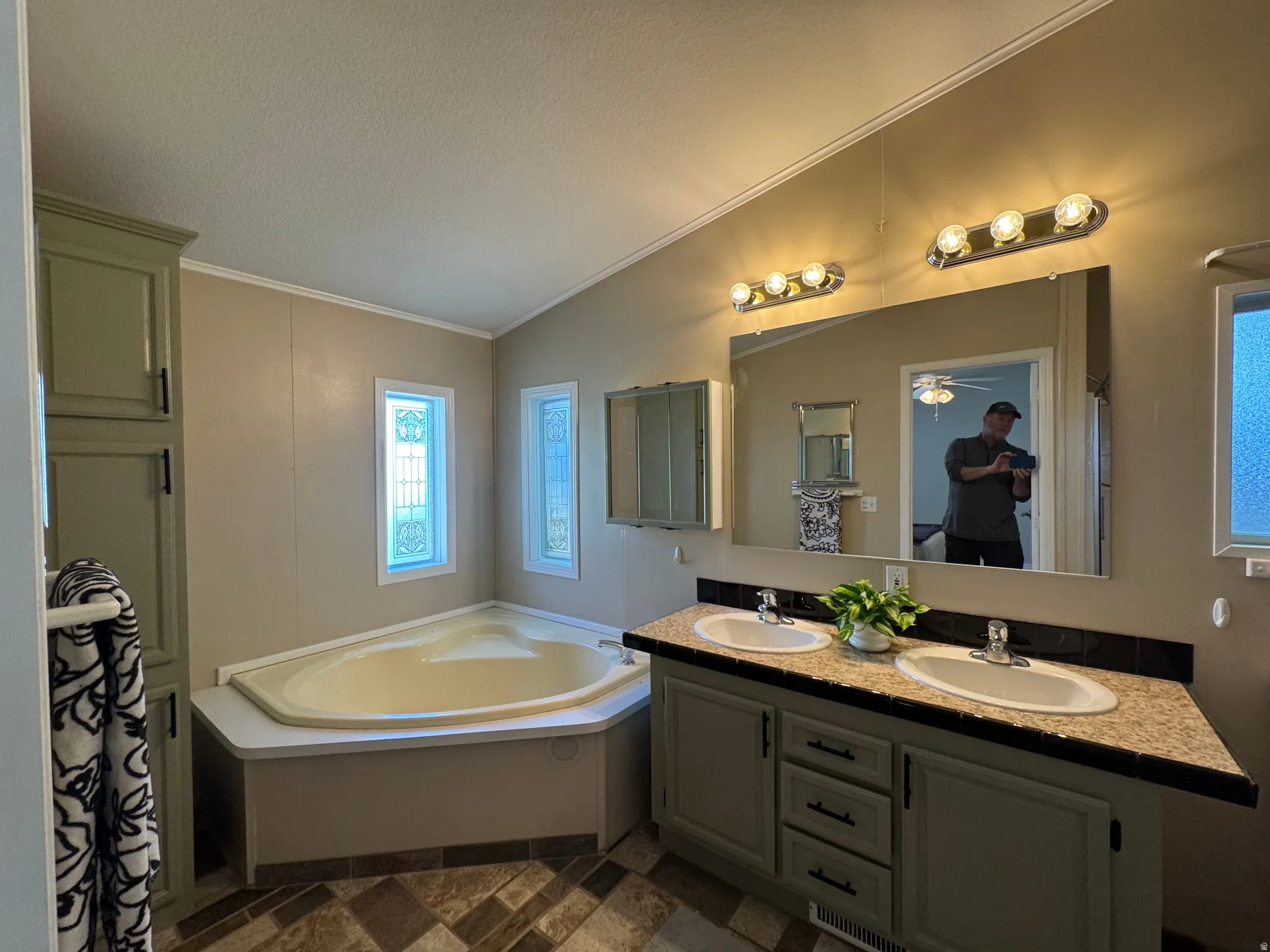 Corner soaking tub with dual decorative windows, complemented by a double vanity featuring an integrated mirror and overhead lighting