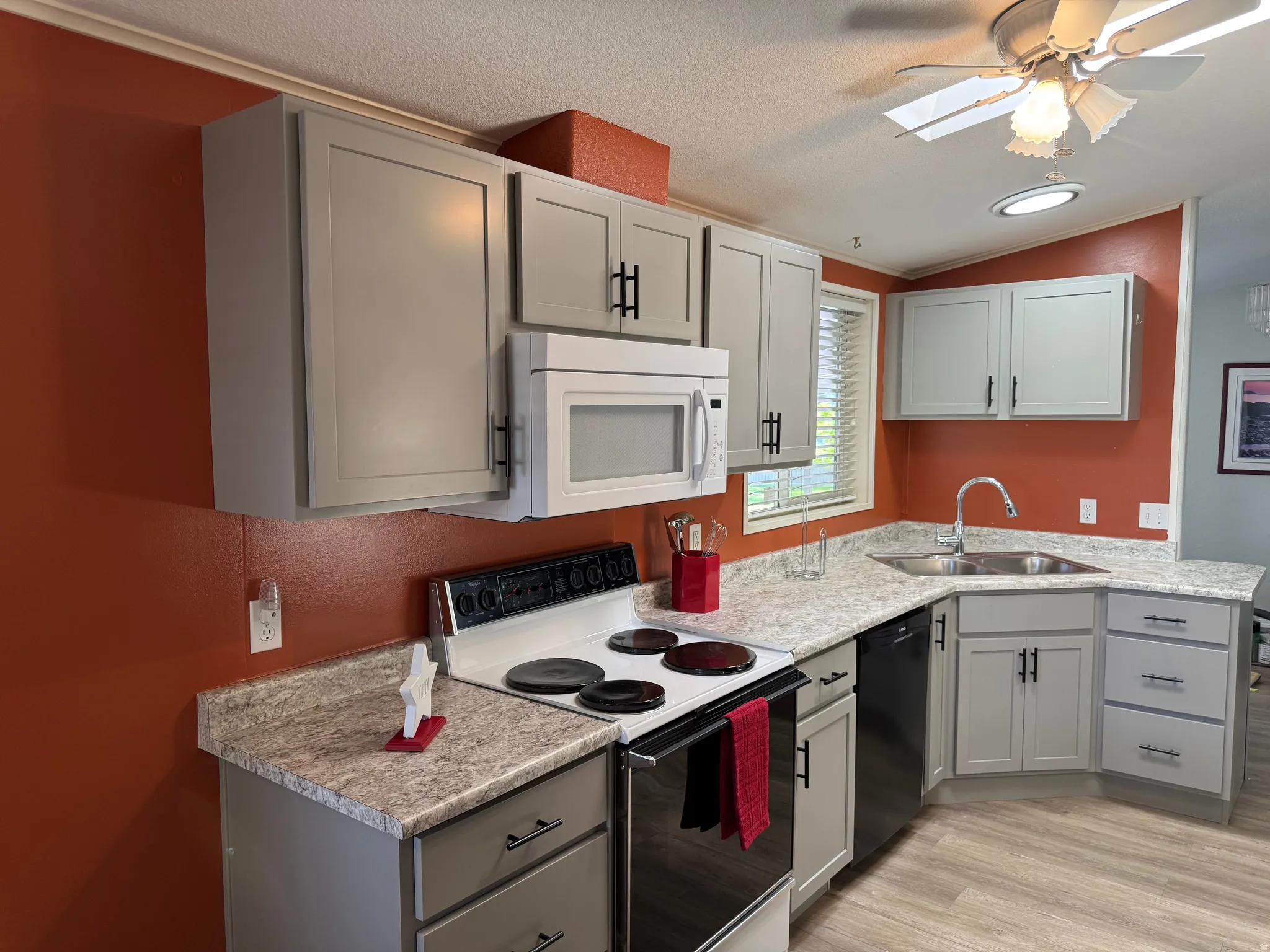 Kitchen featuring gray cabinetry with black hardware, corner sink with gooseneck faucet, white overhead microwave, and a white electric range