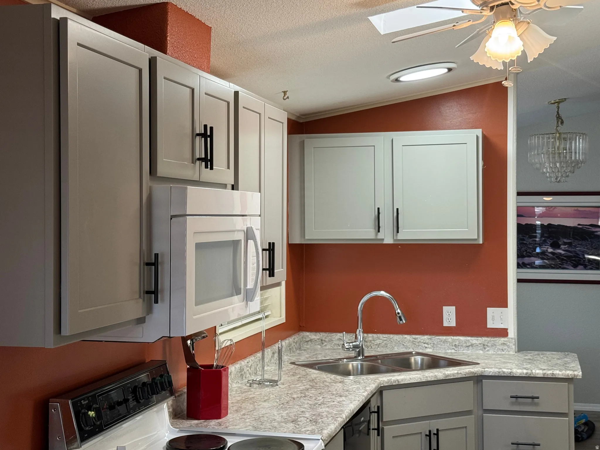 Kitchen featuring light gray shaker-style cabinetry with black hardware, a stainless steel double basin sink with a pull-down faucet, and light-toned countertops