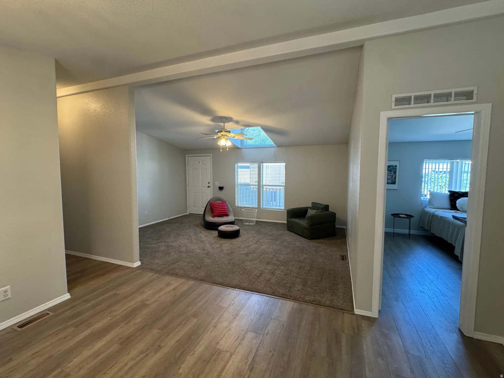 Open-concept living space featuring wood-finish flooring, vaulted ceilings, a ceiling fan, and large windows