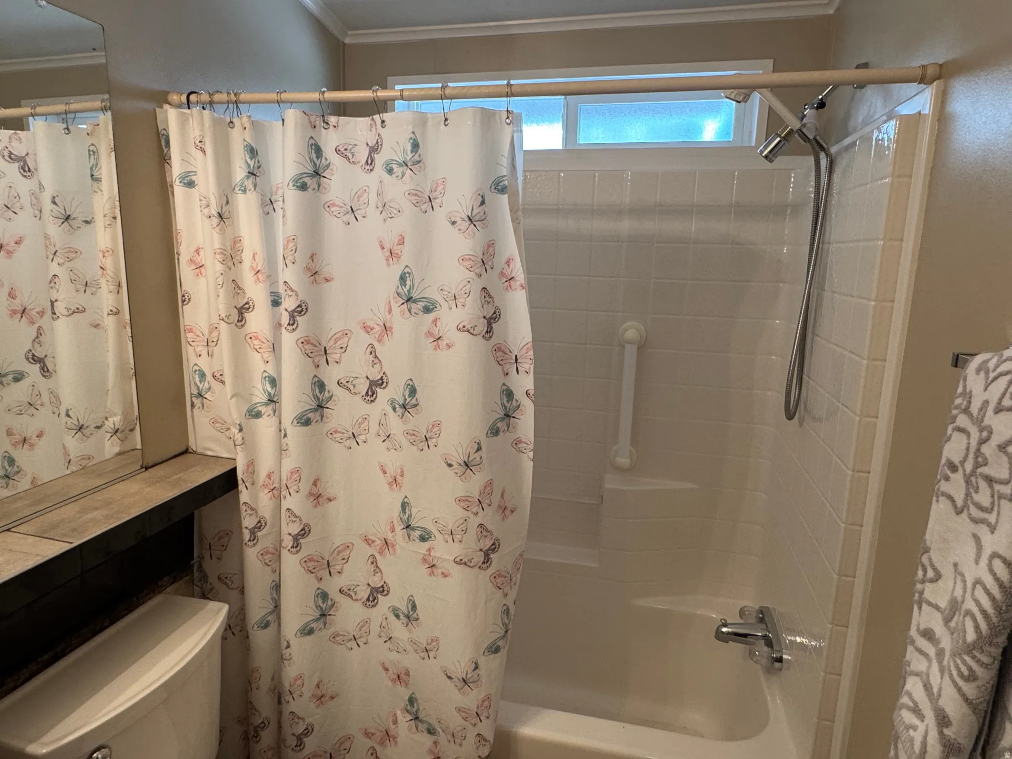 Tub-shower combination featuring a white tile surround, chrome fixtures, and an overhead window