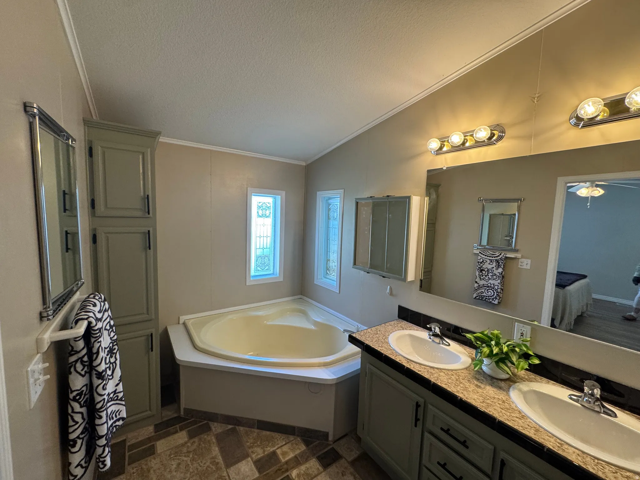 Bathroom with a corner soaking tub, two decorative frosted windows, and a built-in storage cabinet