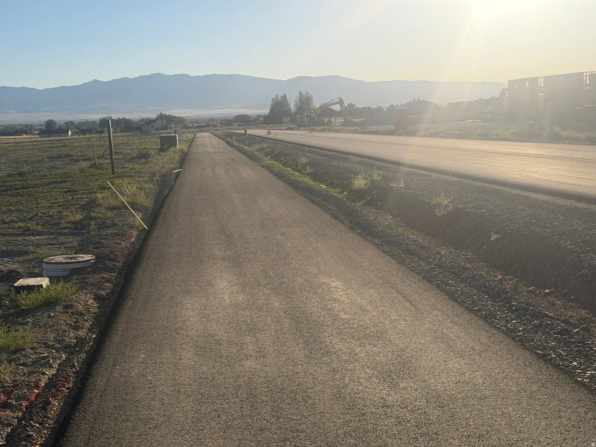 Paved road extending into the distance, bordered by undeveloped land and a distant mountain range