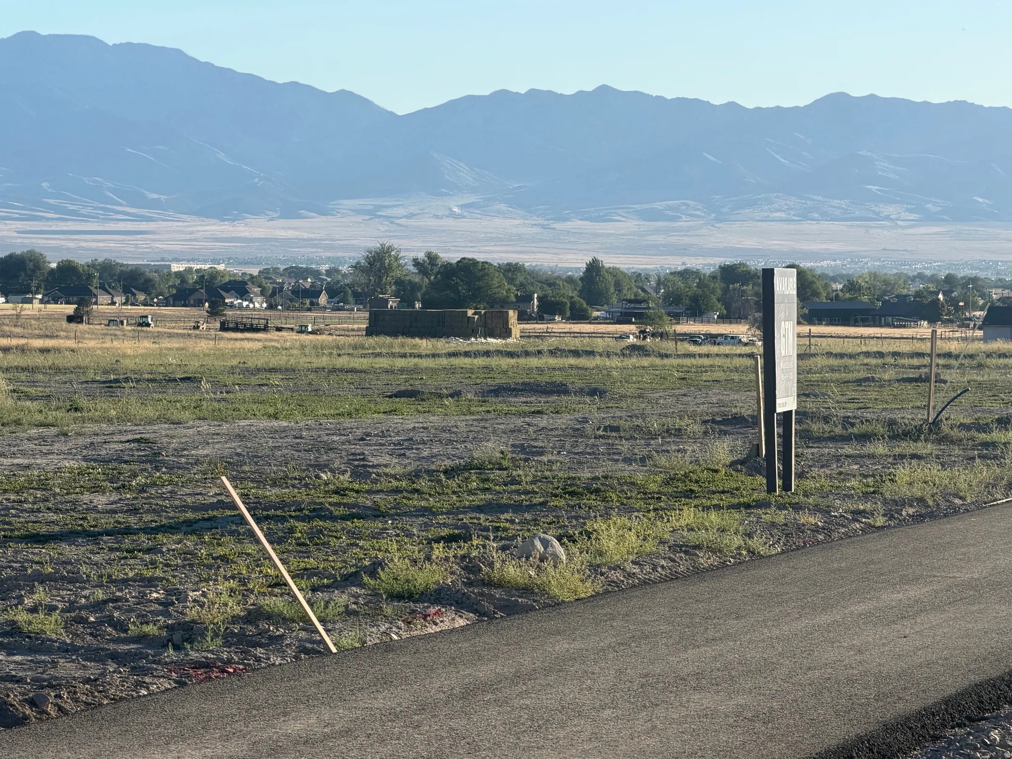 Expansive undeveloped parcel featuring a mountainous backdrop, distant community elements, and an adjacent paved road
