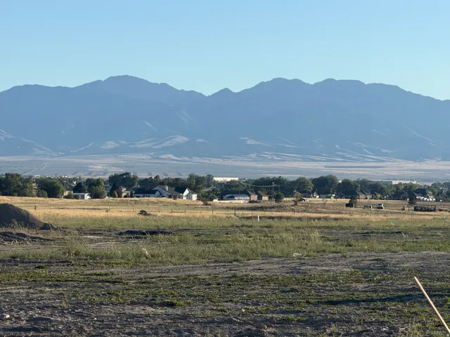 Expansive land parcel featuring natural ground cover, distant residential structures, and a prominent mountain range backdrop