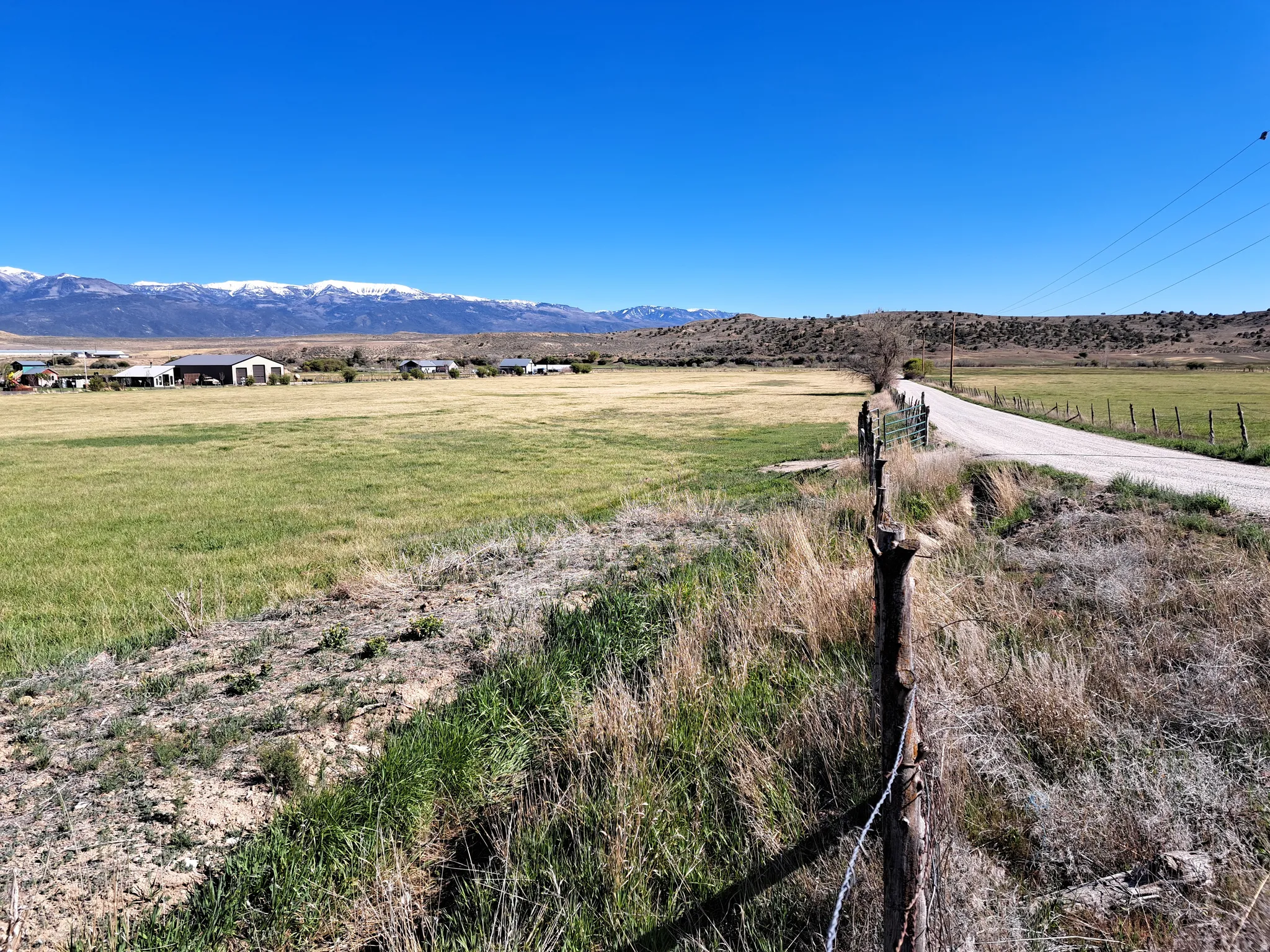 Expansive agricultural land featuring a gravel road, wire fencing, and distant snow-capped mountains