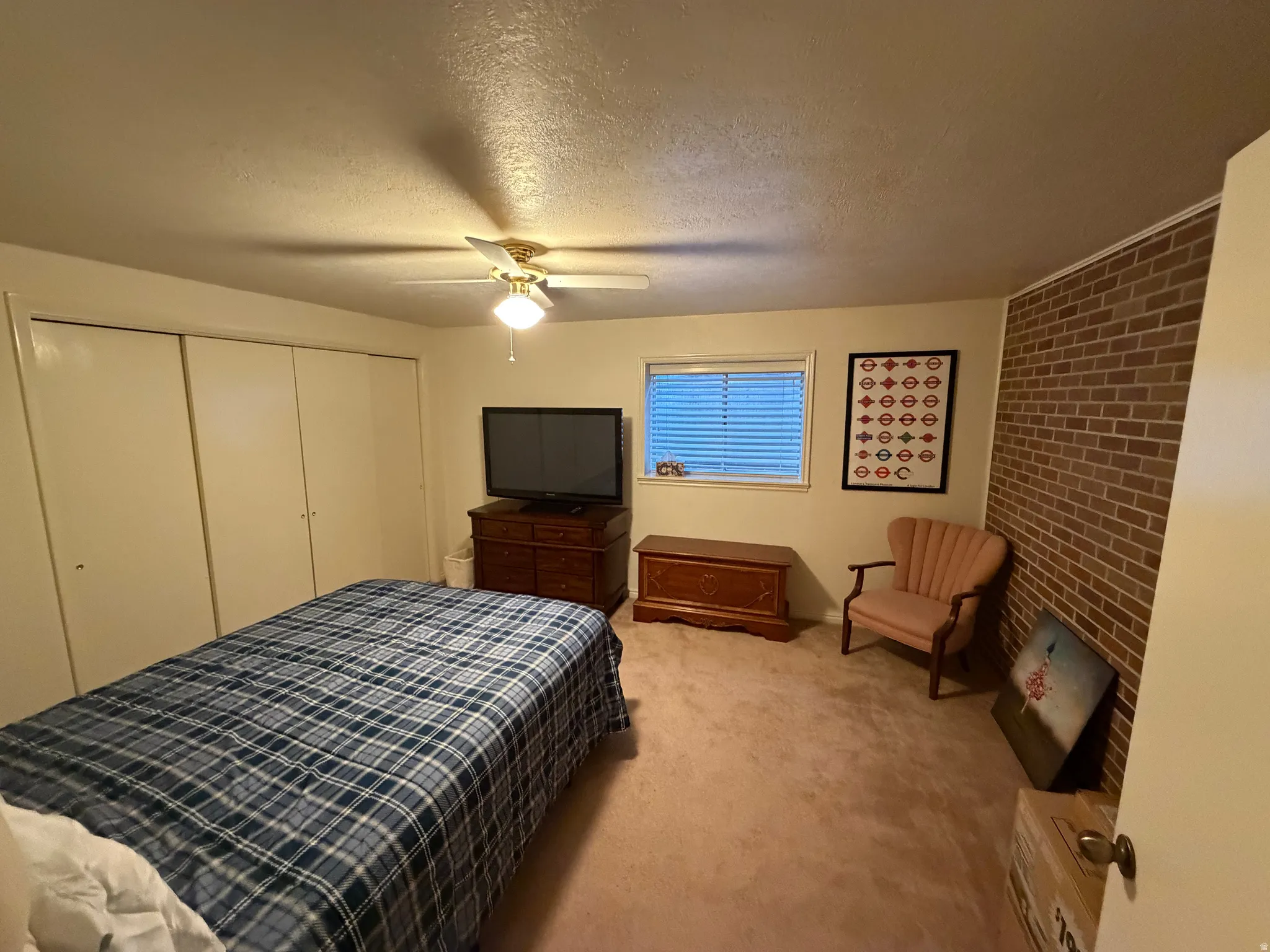 Bedroom featuring a partial brick accent wall, neutral carpeting, and a ceiling fan with integrated lighting