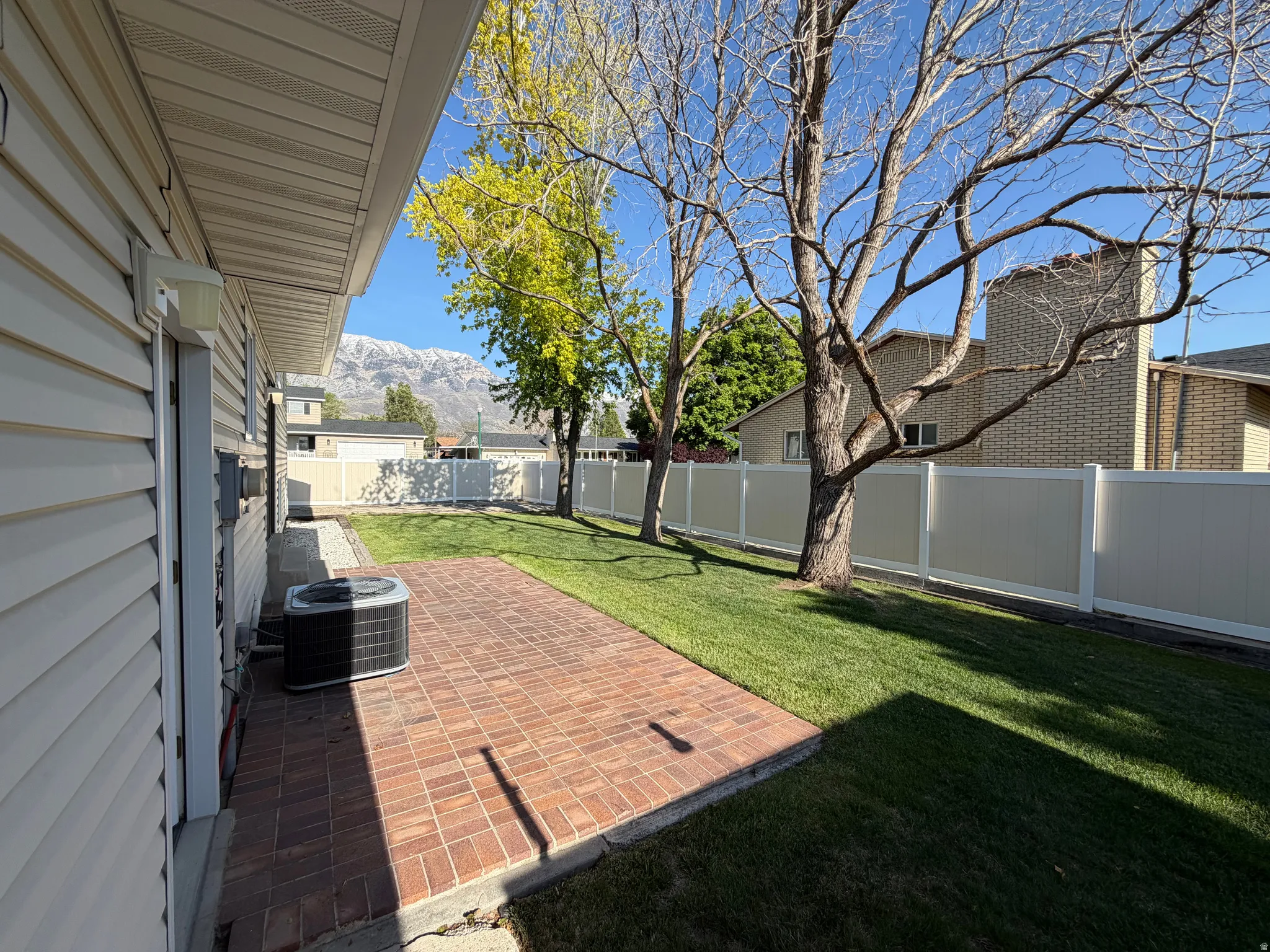Expansive backyard featuring a red brick patio, manicured lawn, full privacy fencing, mature trees, and mountain scenery
