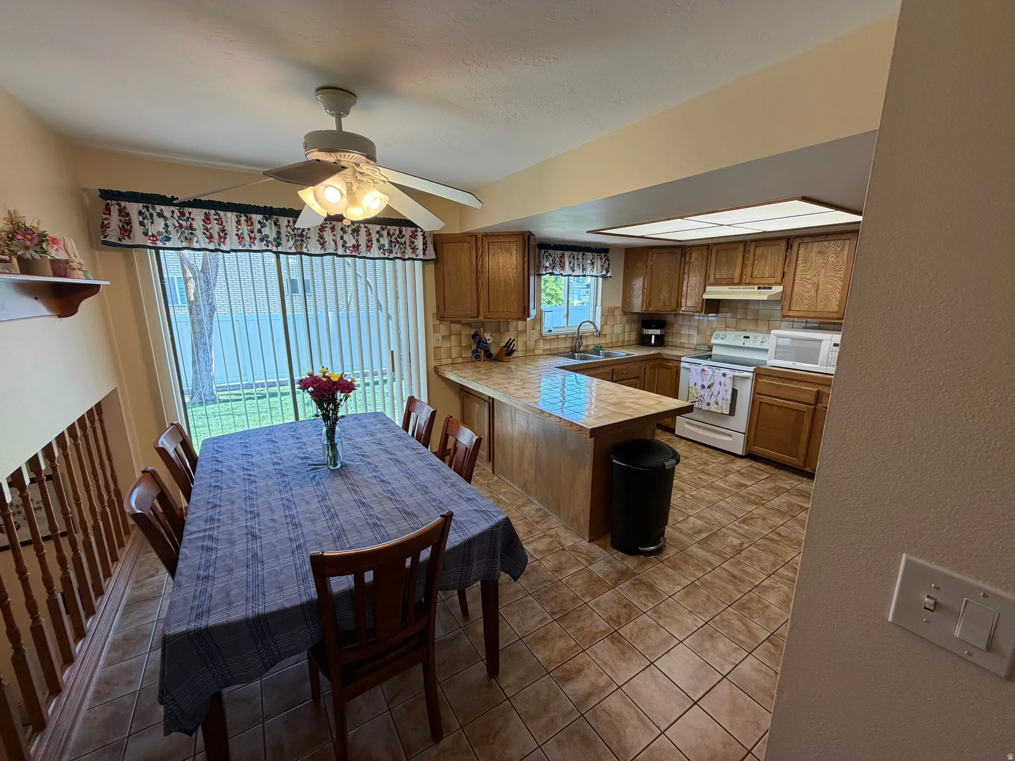 Kitchen and dining area featuring warm wood cabinetry, a tiled backsplash, and light-toned countertops