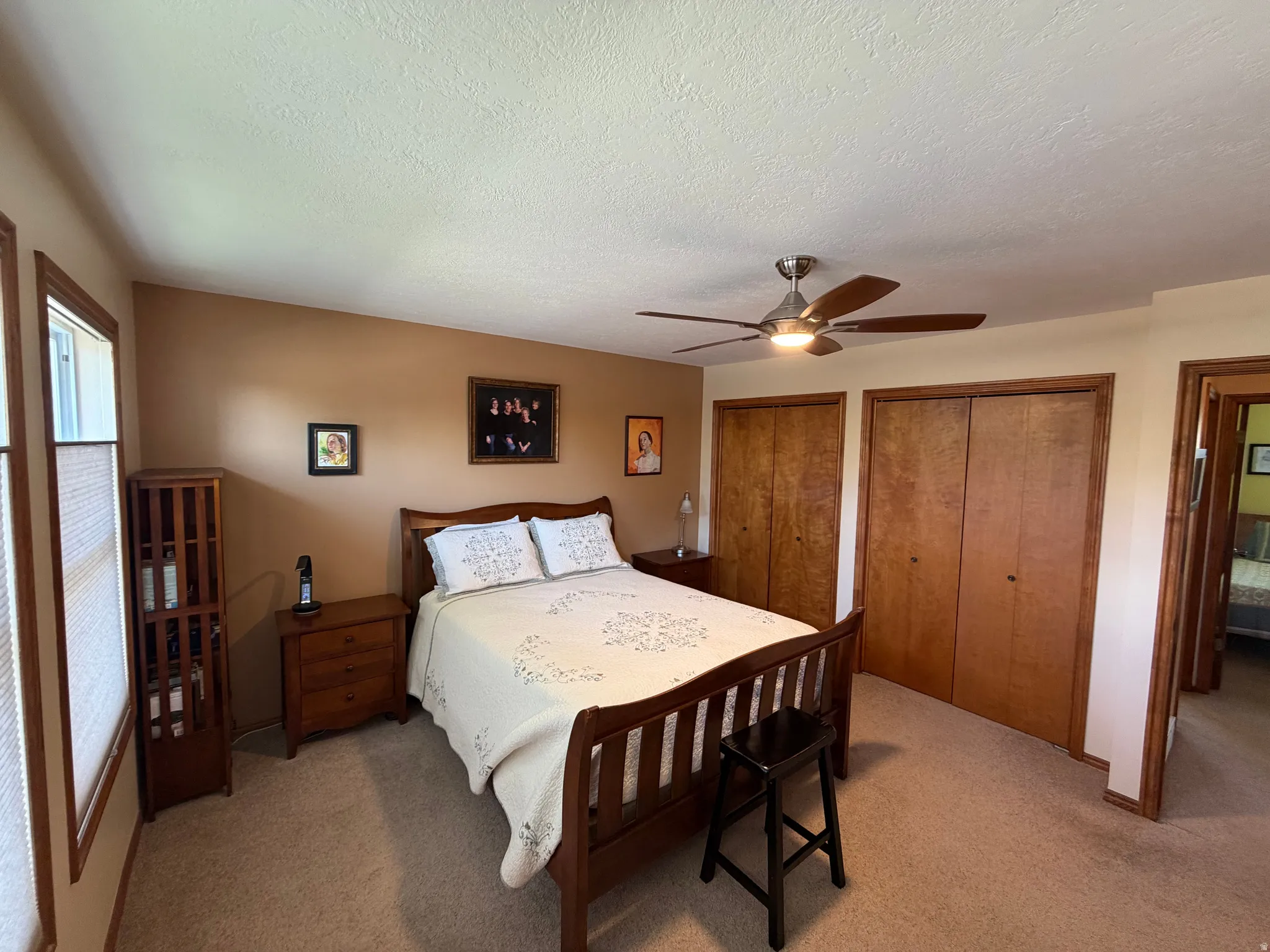 Carpeted bedroom featuring a ceiling fan with integrated lighting, two windows with blinds, and two wood-finish bi-fold closet doors